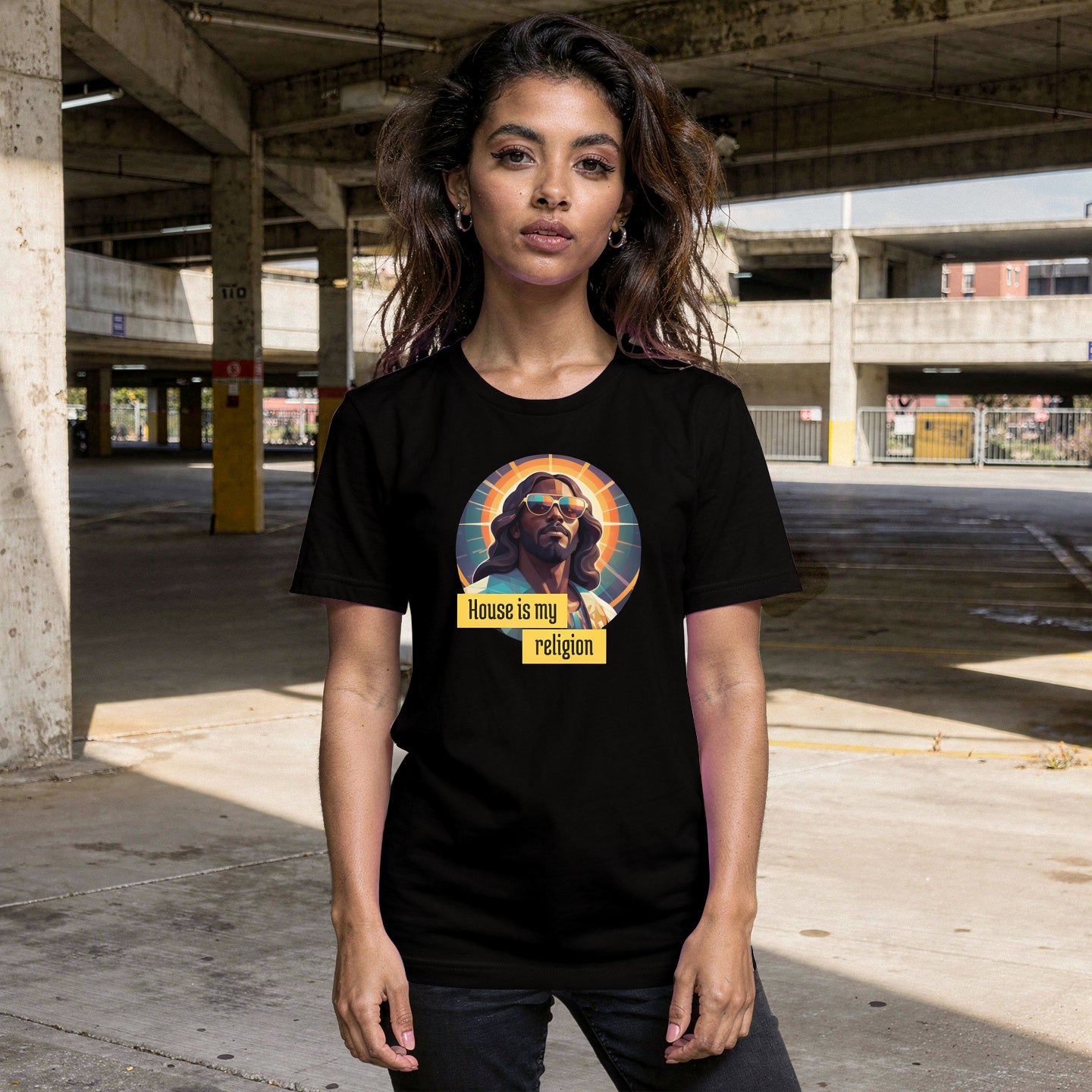 A person wearing a black t-shirt with a graphic design of Funky Jaysus with the wording 'House is my religion' in an empty car park.