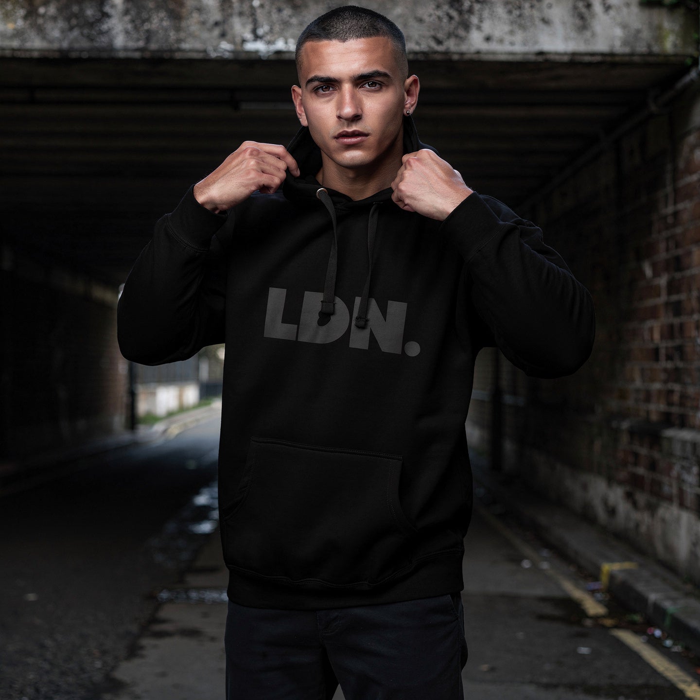 Unisex Hoodie - Black hoodie with tonal “LDN.” graphic worn by male model — soft fleece lining, relaxed streetwear silhouette, perfect for layering in cooler seasons.