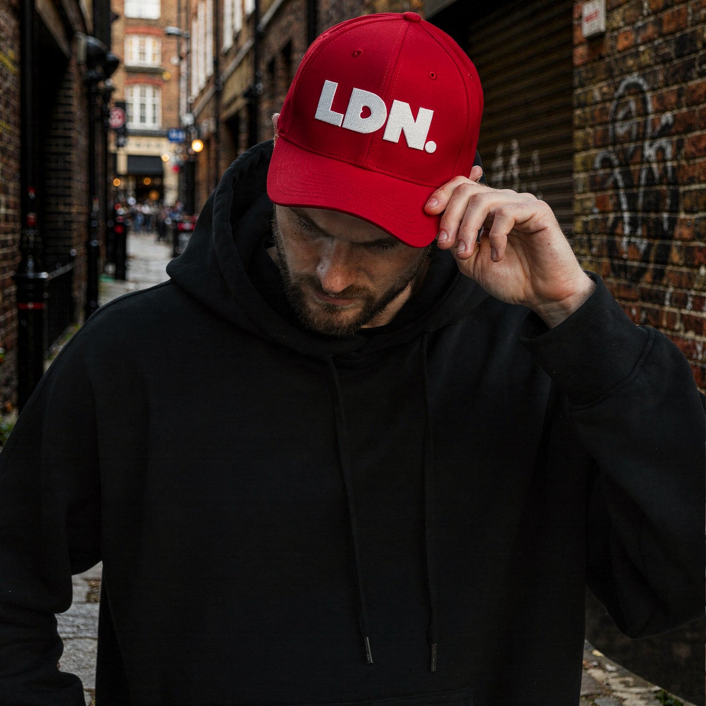 Man wearing a black hoodie and red cap with 'LDN.' text in an urban setting