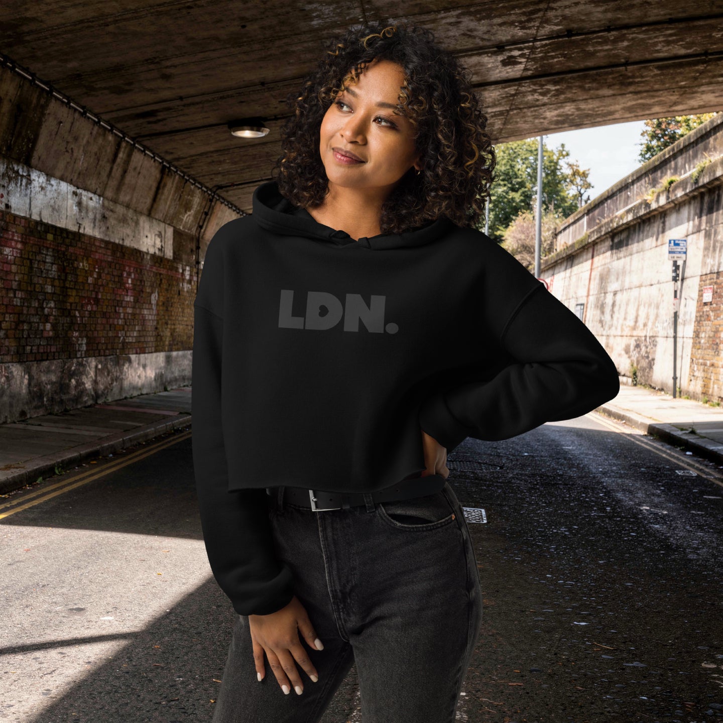 Model wearing a cropped hoodie with tonal “LDN.” graphic. Hoodie features dropped shoulders, raw hem, and dyed-to-match drawstrings. Made from cotton-poly fleece blend for soft comfort and relaxed fit. A minimal, modern streetwear piece.