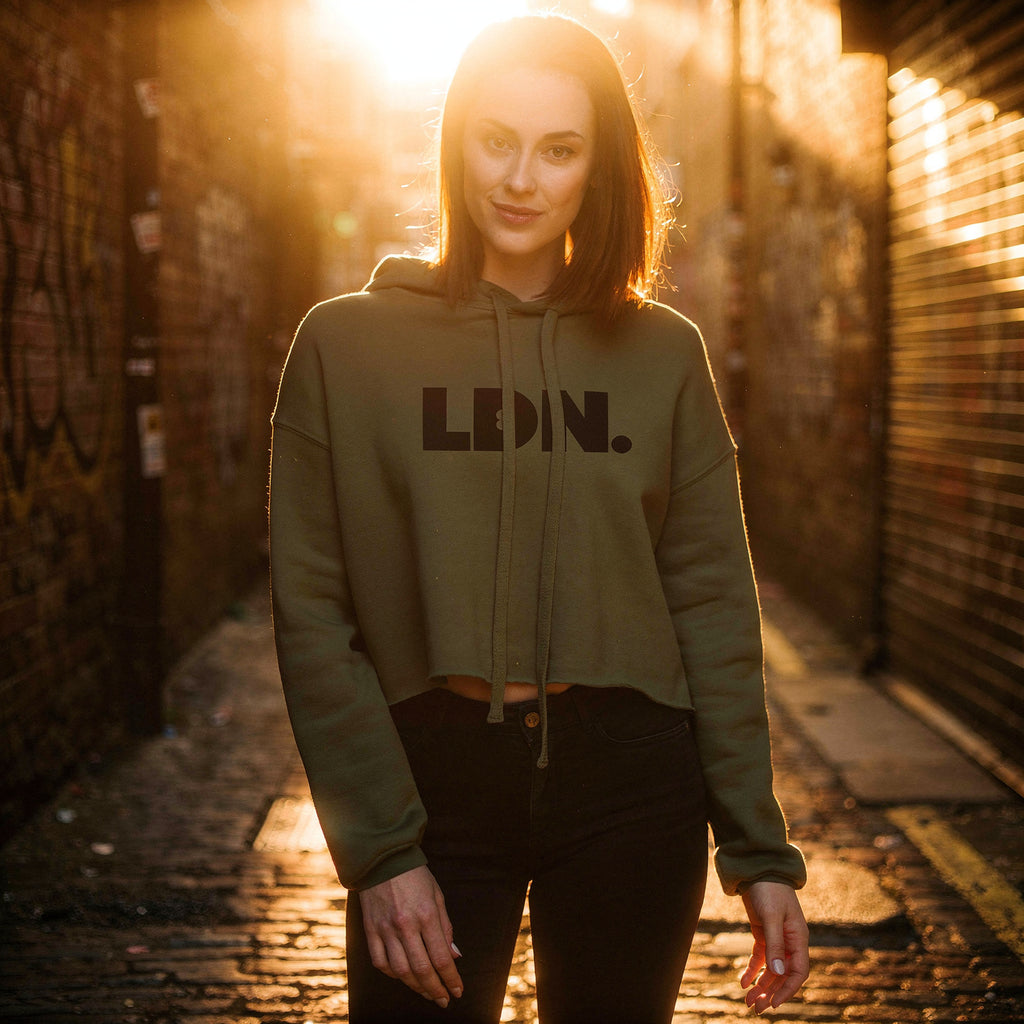 Model wearing a cropped hoodie with tonal “LDN.” graphic. Hoodie features dropped shoulders, raw hem, and dyed-to-match drawstrings. Made from cotton-poly fleece blend for soft comfort and relaxed fit. A minimal, modern streetwear piece.