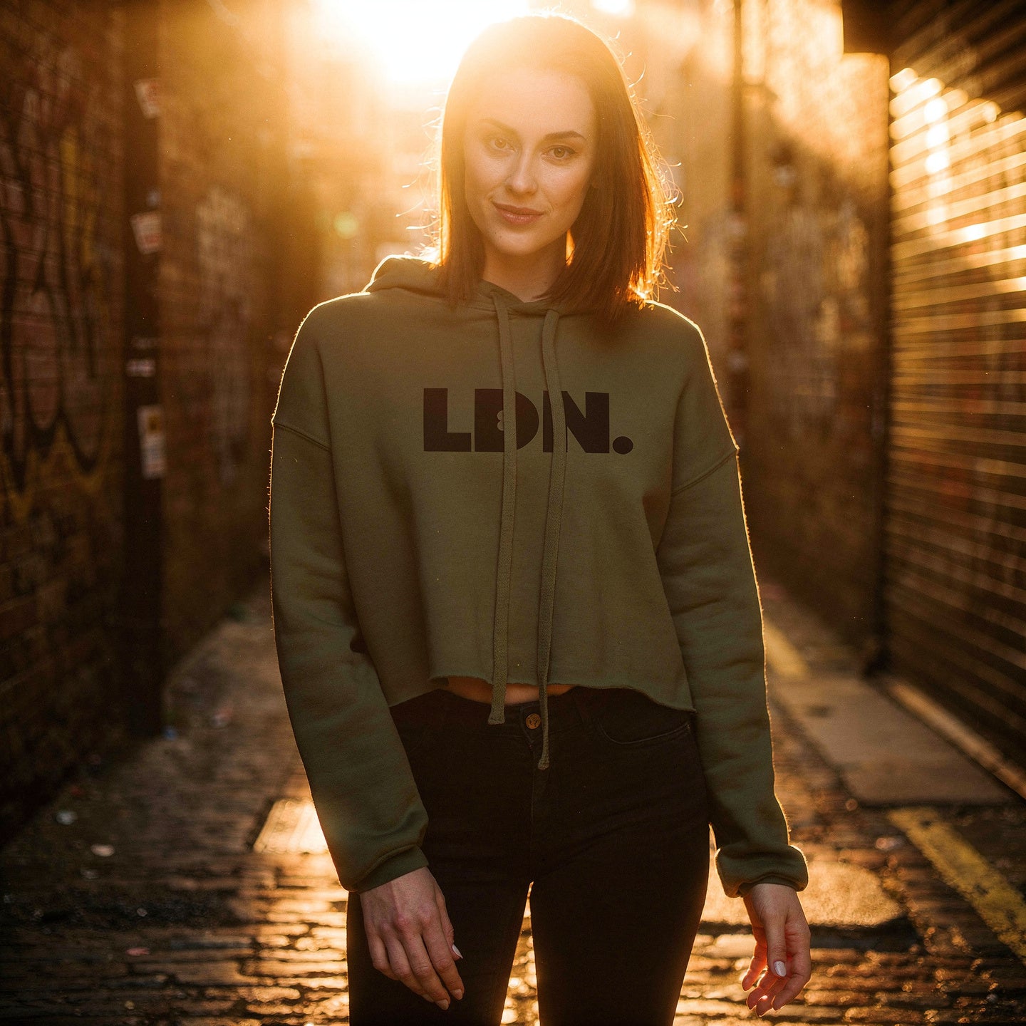 Model wearing a cropped hoodie with tonal “LDN.” graphic. Hoodie features dropped shoulders, raw hem, and dyed-to-match drawstrings. Made from cotton-poly fleece blend for soft comfort and relaxed fit. A minimal, modern streetwear piece.