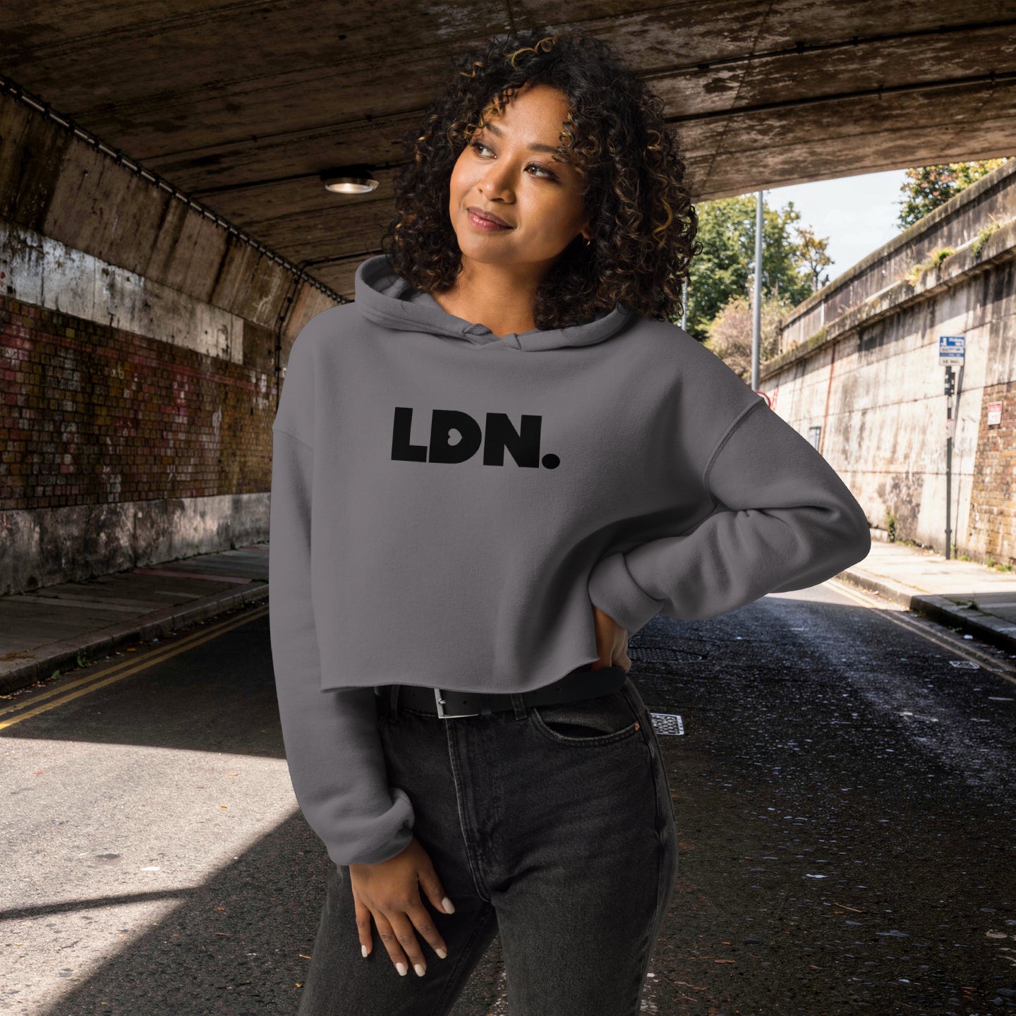 Model wearing a cropped hoodie with tonal “LDN.” graphic. Hoodie features dropped shoulders, raw hem, and dyed-to-match drawstrings. Made from cotton-poly fleece blend for soft comfort and relaxed fit. A minimal, modern streetwear piece.