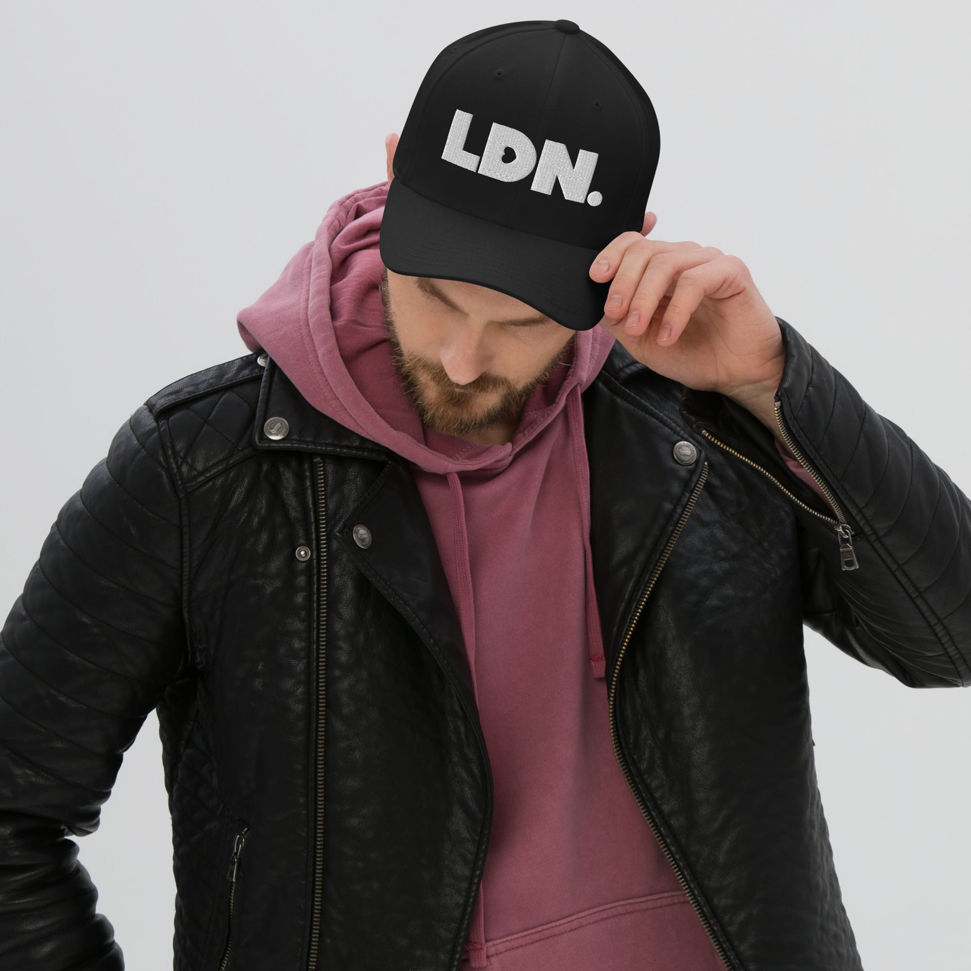 Person wearing a black cap with 'LDN.' text, black leather jacket, and pink hoodie on a light gray background