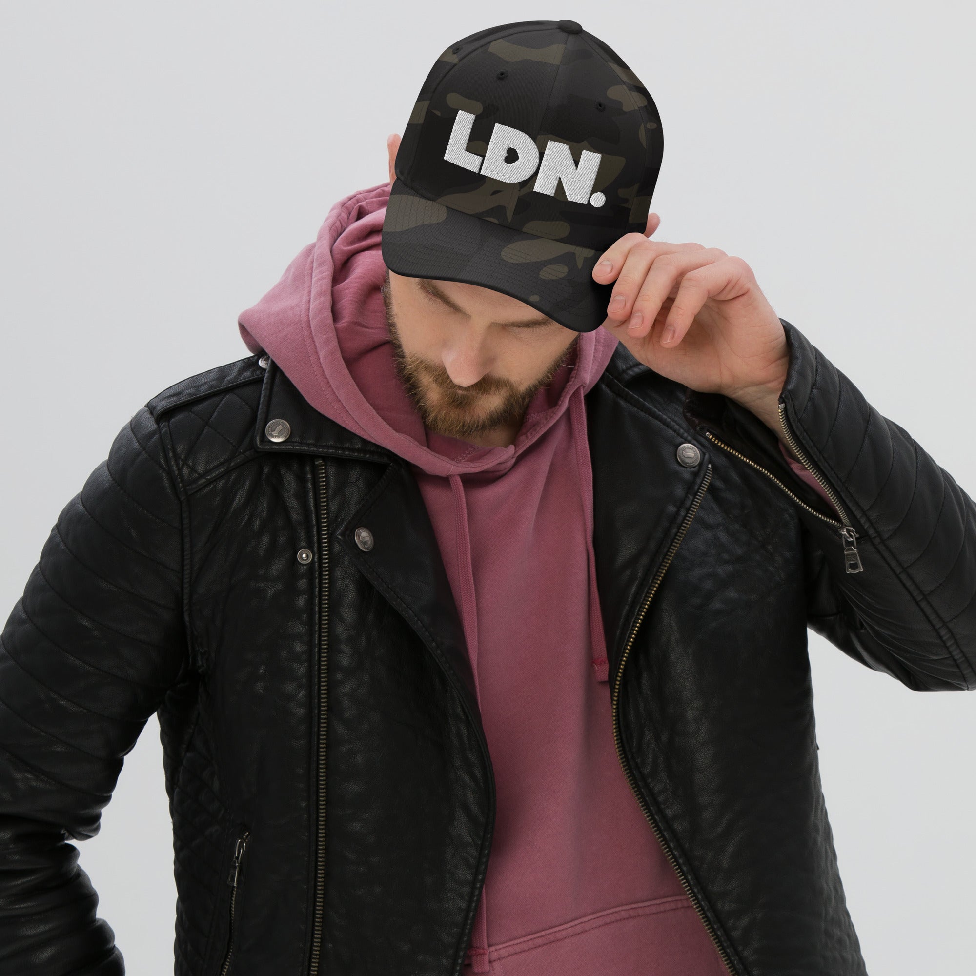 Person wearing a black cap with 'LDN.' text, black leather jacket, and pink hoodie on a light gray background