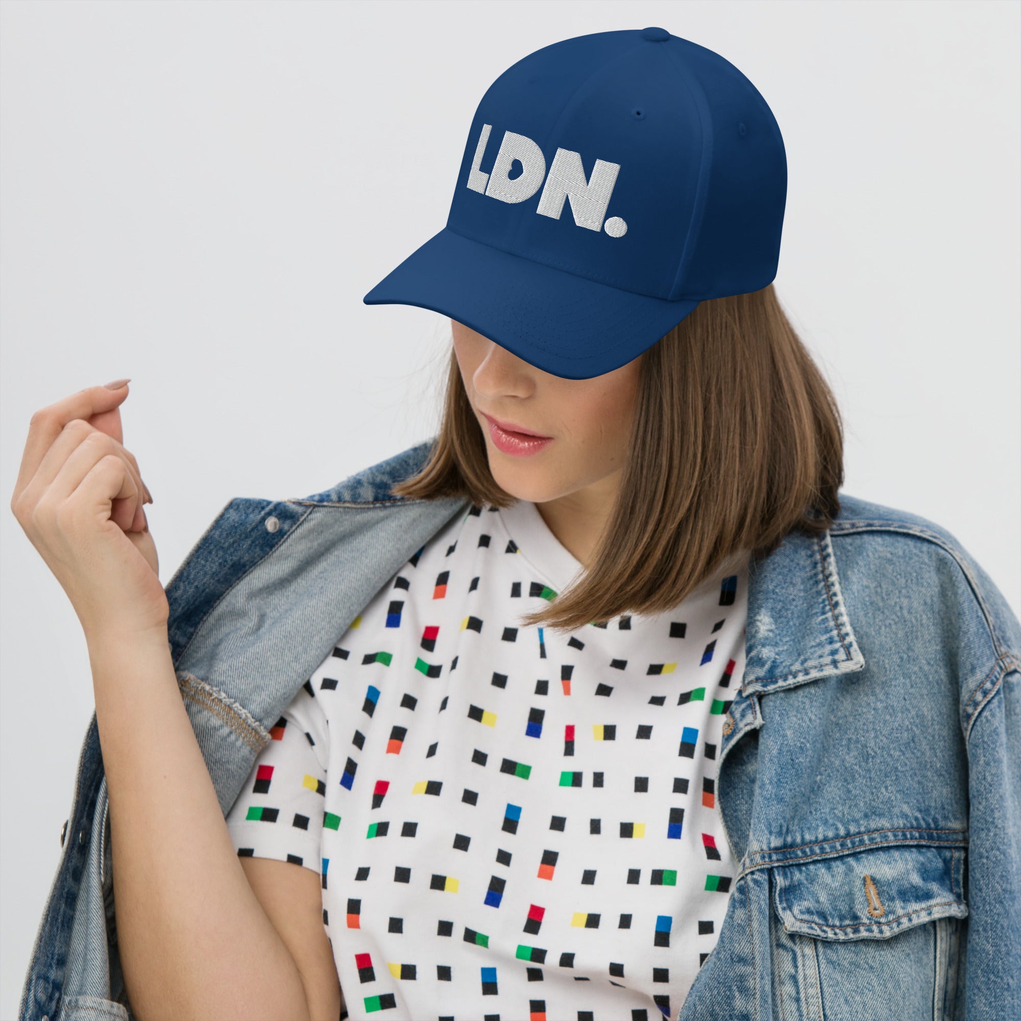 Person wearing a blue cap with 'LDN.' text, white shirt with colorful pattern, and denim jacket on a light gray background