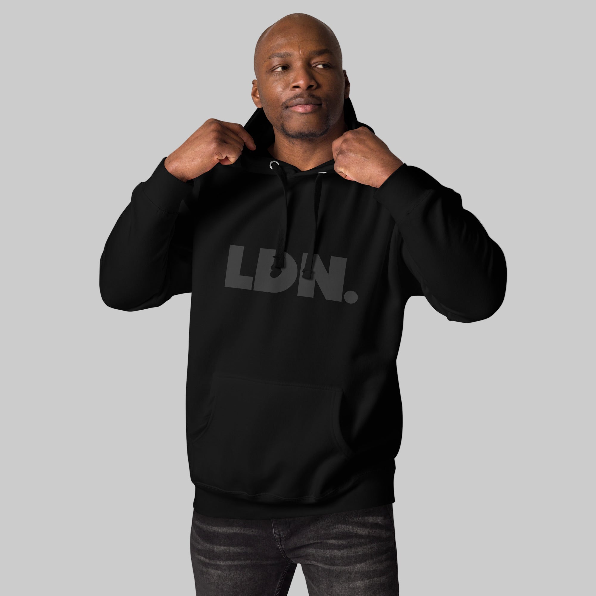 Unisex Hoodie - Black hoodie with tonal “LDN.” graphic worn by male model — soft fleece lining, relaxed streetwear silhouette, perfect for layering in cooler seasons.