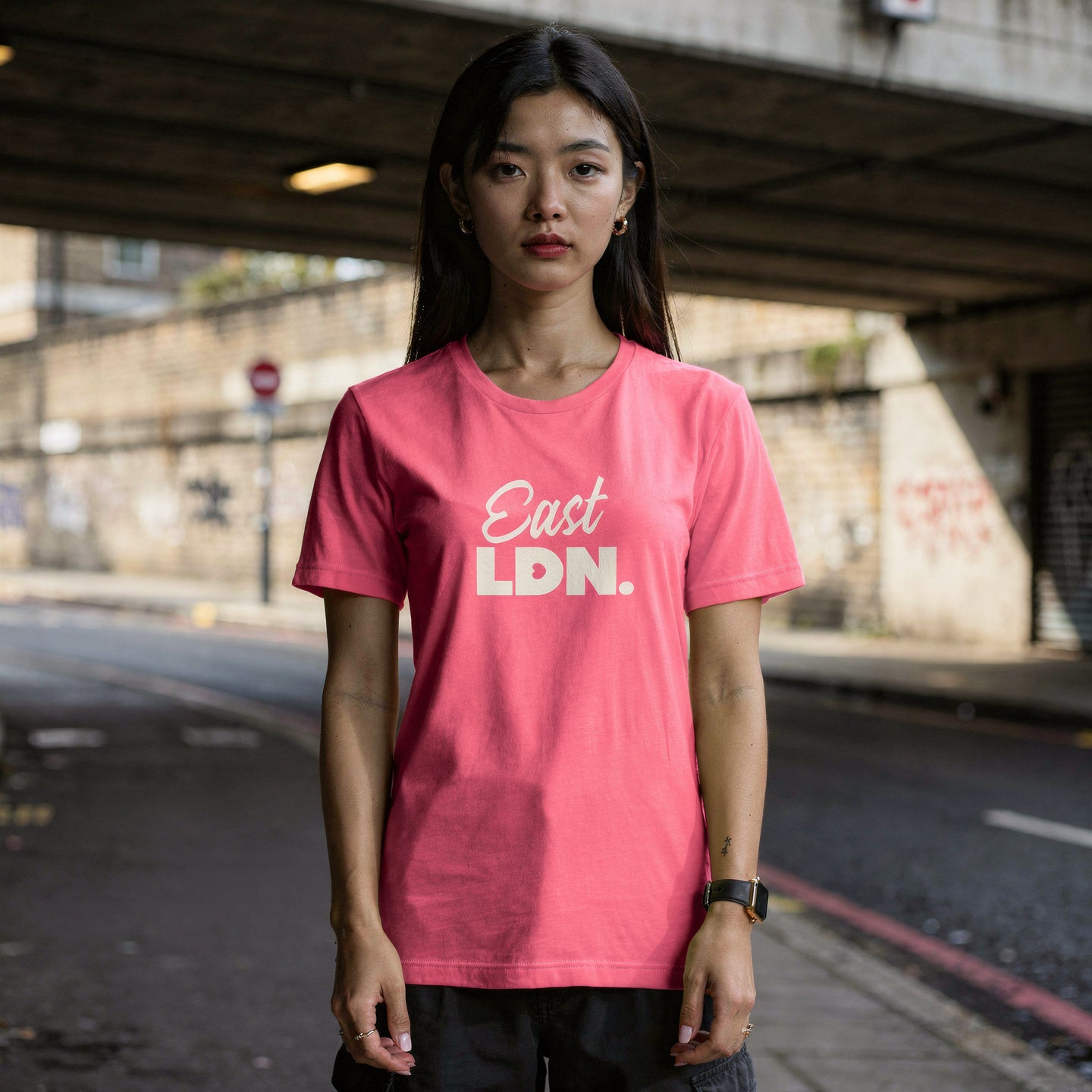 Person wearing a pink 'East LDN' t-shirt standing on a street.