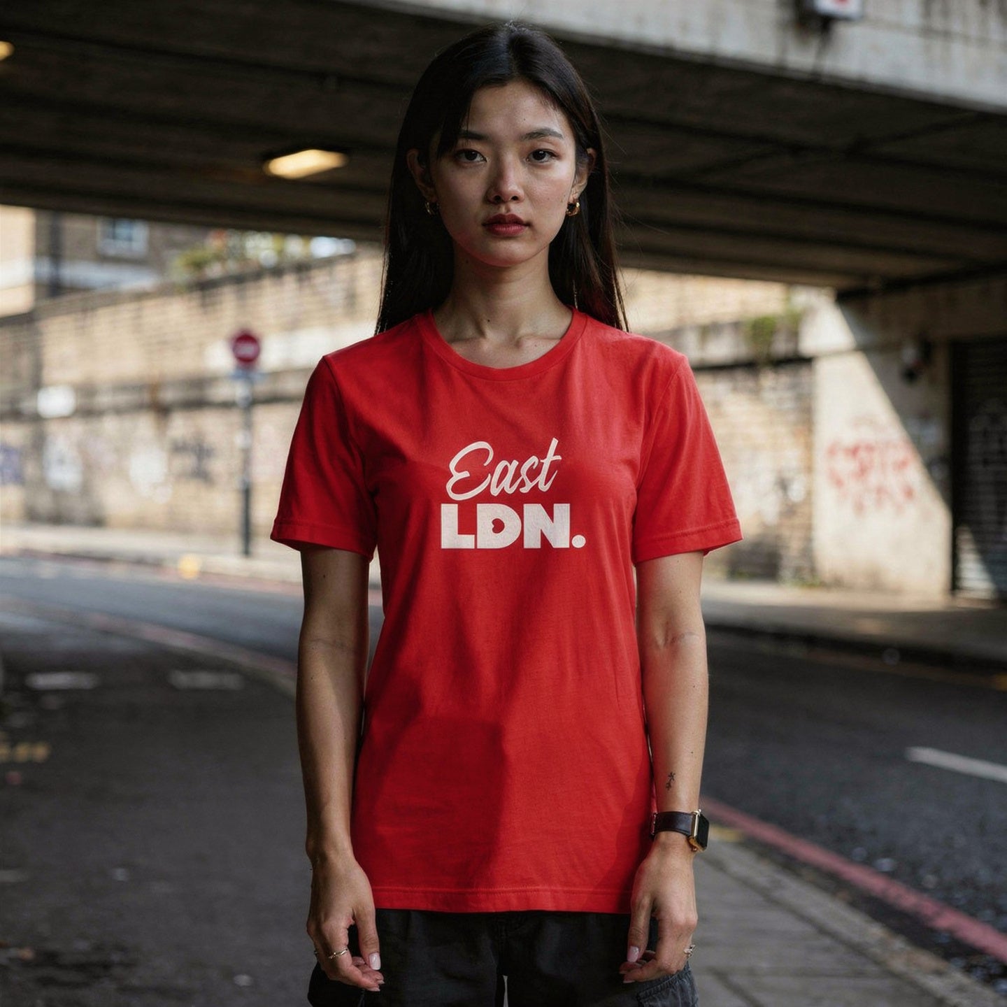 Person wearing a red 'East LDN' t-shirt standing under an overpass.