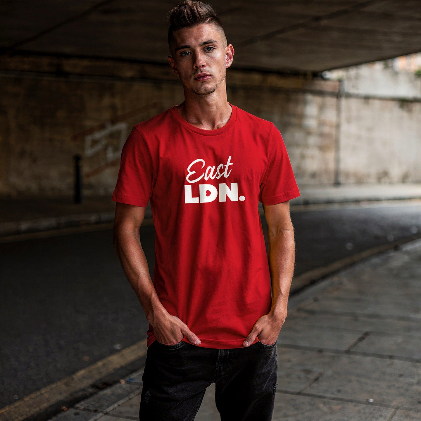 Person wearing a red t-shirt with 'East LDN.' text standing under a bridge.