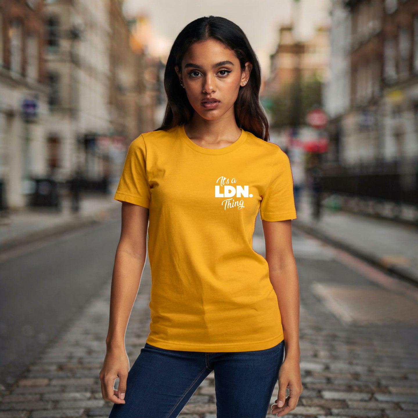 Woman wearing a heather yellow gold t-shirt with 'It's a Ldn Thing' text on a city street.