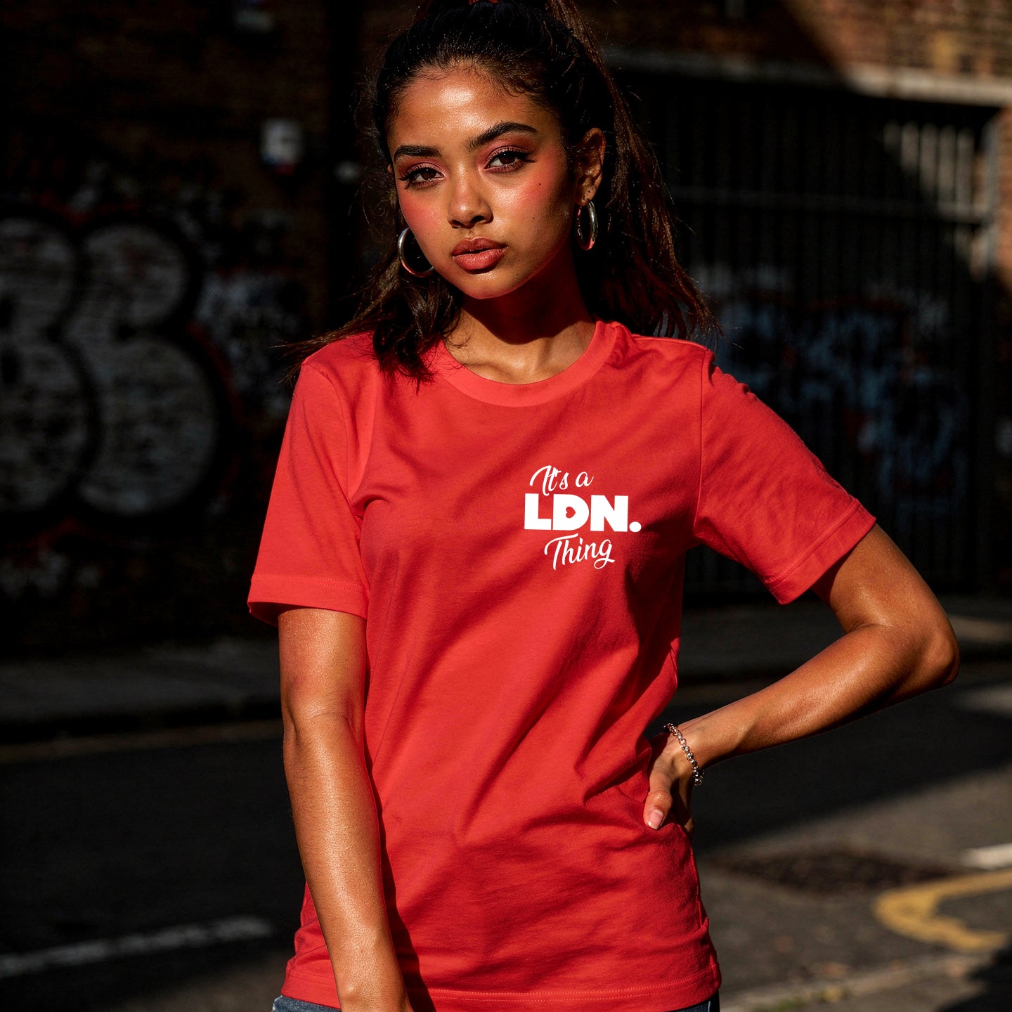 Person wearing a red t-shirt with 'It's a LDN Thing' text, standing against a dark background.