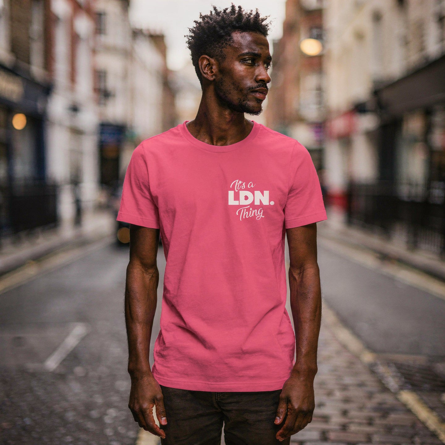Man wearing a pink t-shirt with 'It's a LDN Thing' text on a city street.