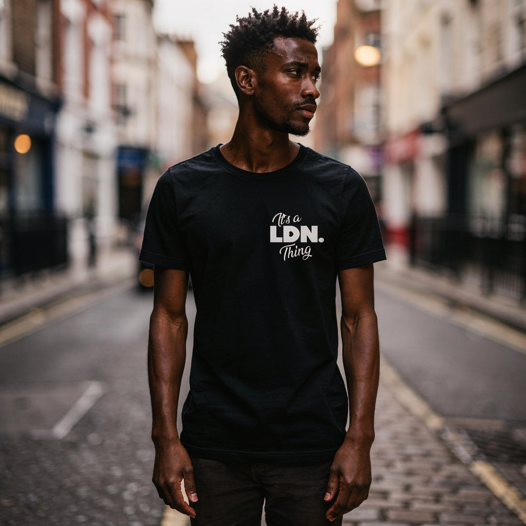 Man wearing a black t-shirt with 'It's a LDN Thing' text on a city street.