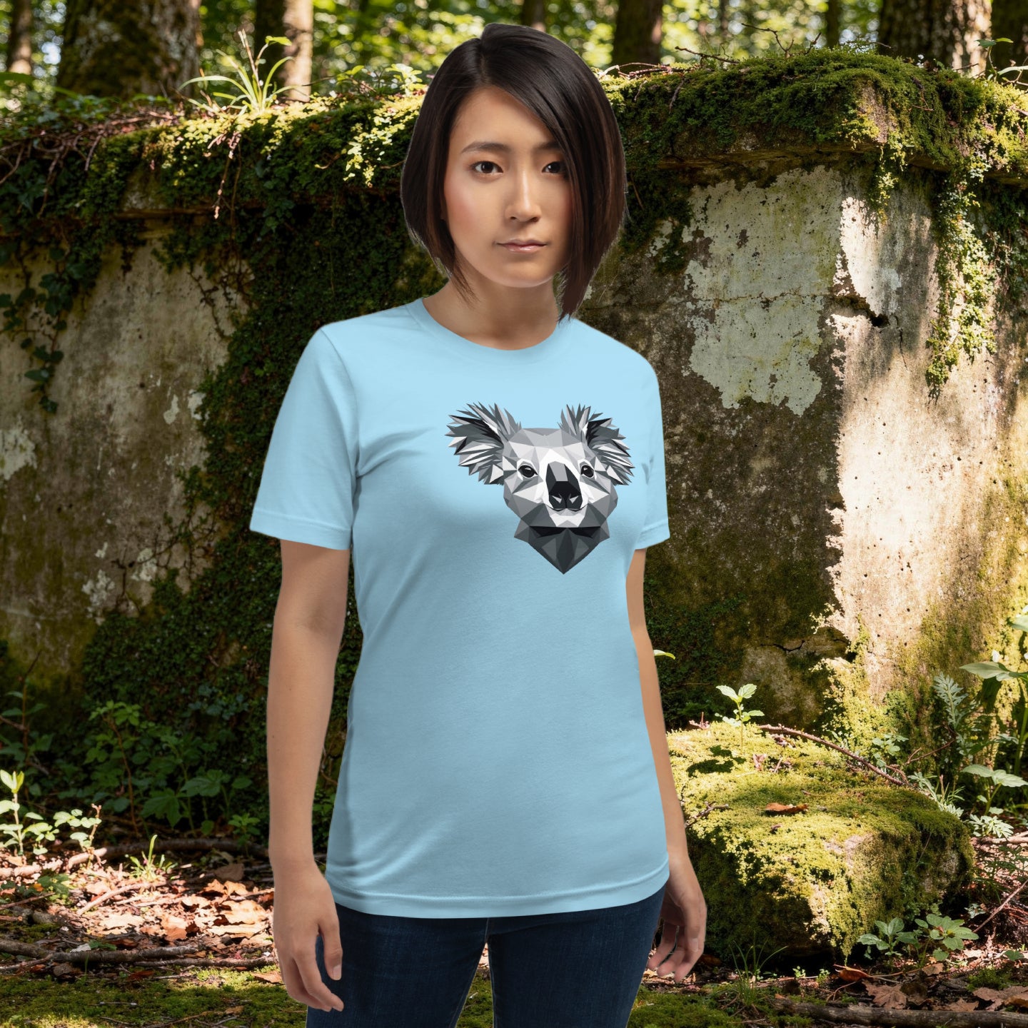 Person wearing a black t-shirt with a koala design, standing in a forest next to a large wall
