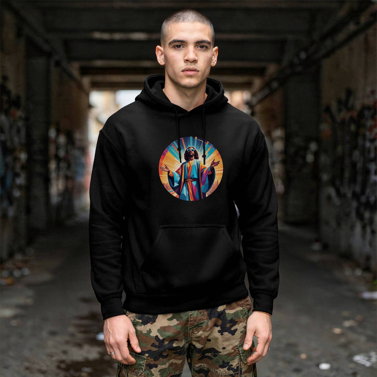 A man wearing a black pullover hoodie with a colorful circular graphic print on the chest, standing in a dark, graffiti-covered alleyway.