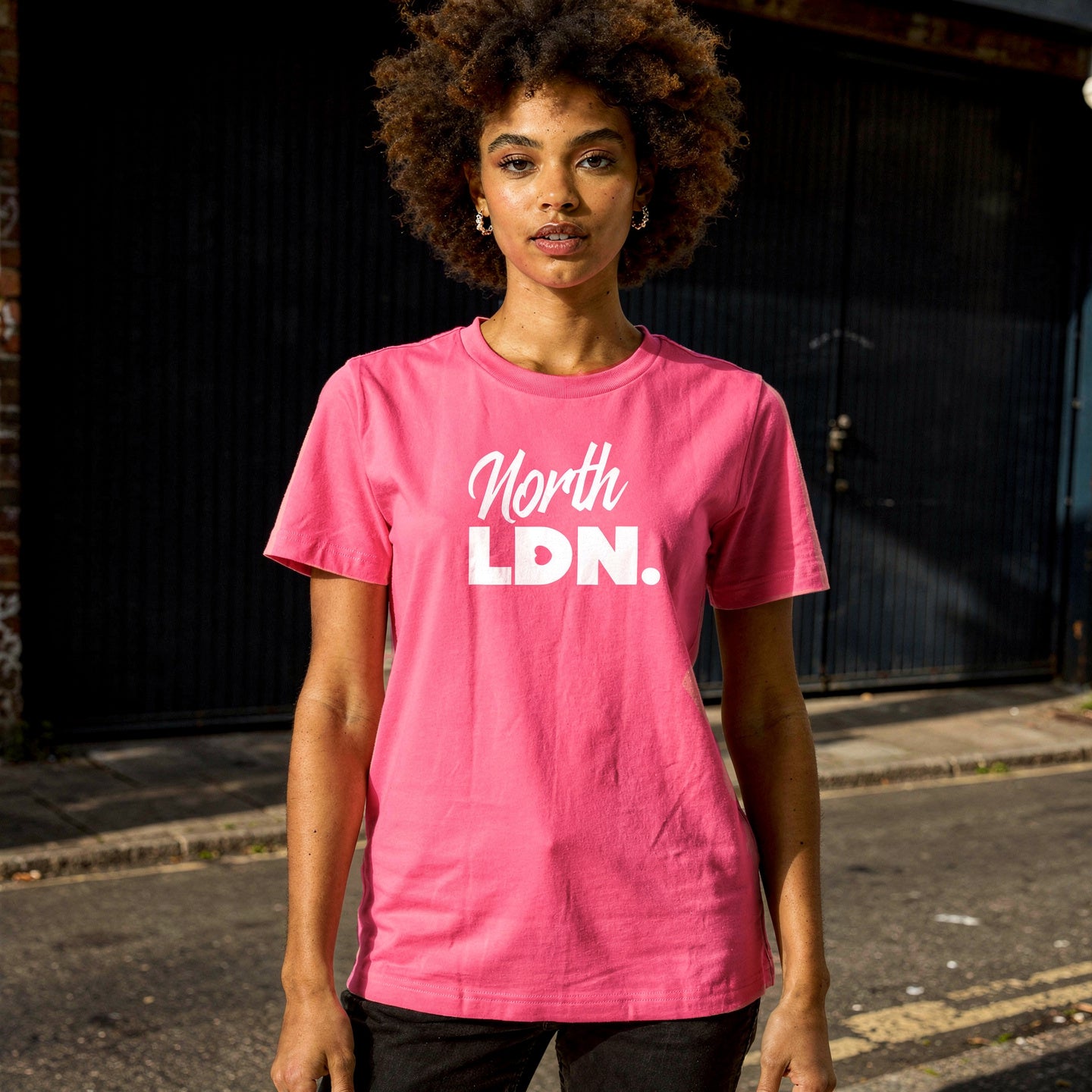 Person wearing a pink 'North LDN' t-shirt standing on a street.