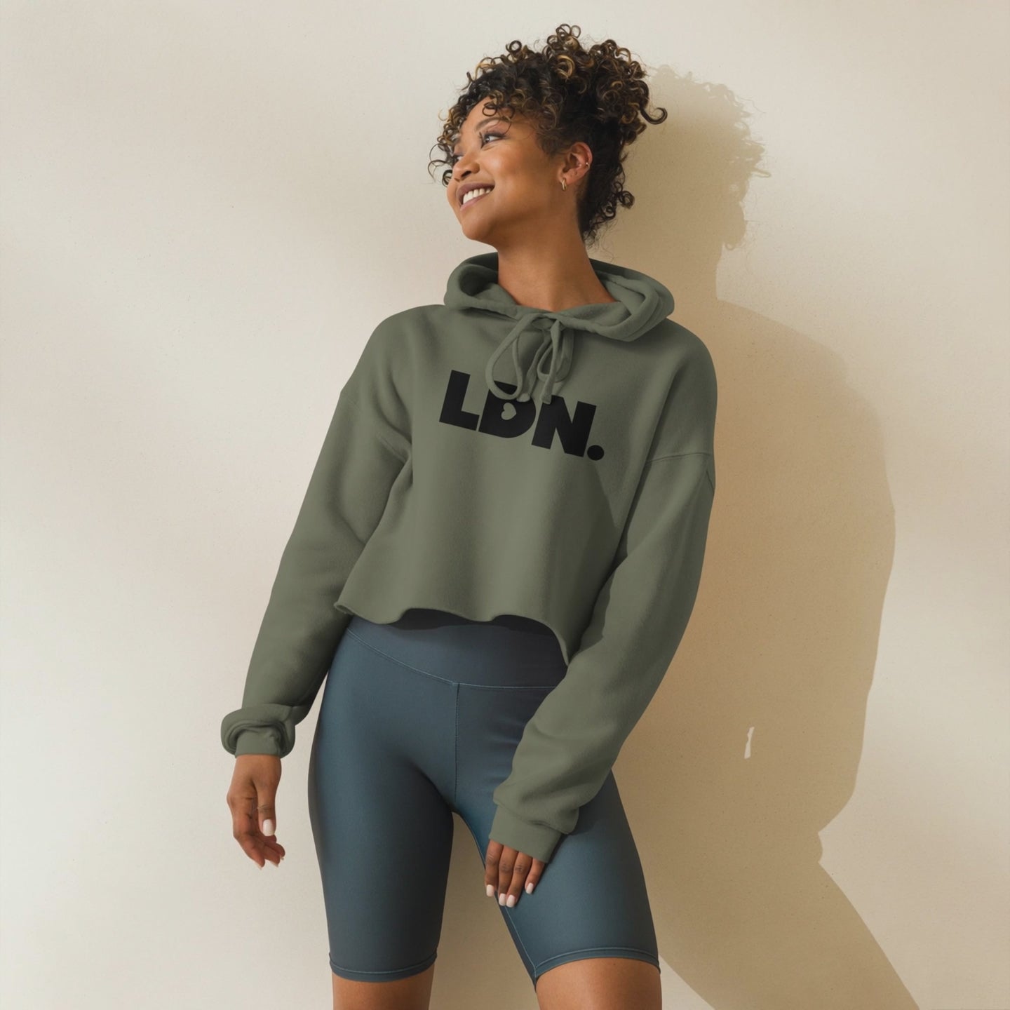 Model wearing a cropped hoodie with tonal “LDN.” graphic. Hoodie features dropped shoulders, raw hem, and dyed-to-match drawstrings. Made from cotton-poly fleece blend for soft comfort and relaxed fit. A minimal, modern streetwear piece.