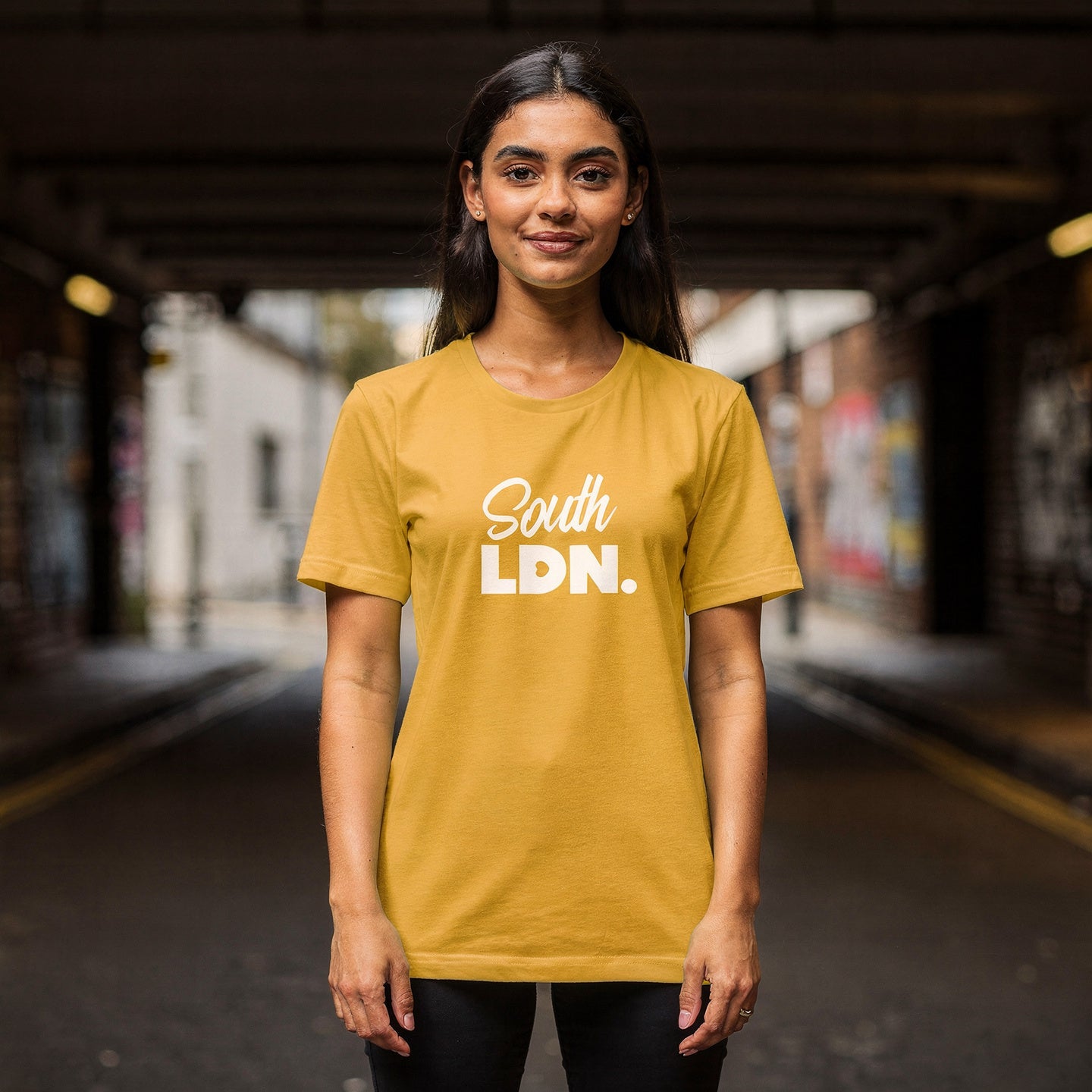 Woman wearing a yellow 'South LDN.' t-shirt standing on a street.
