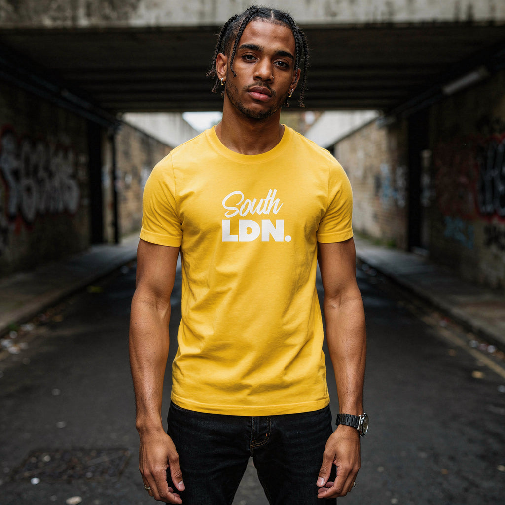 Man wearing a yellow 'South LDN' t-shirt standing in an urban setting with graffiti.