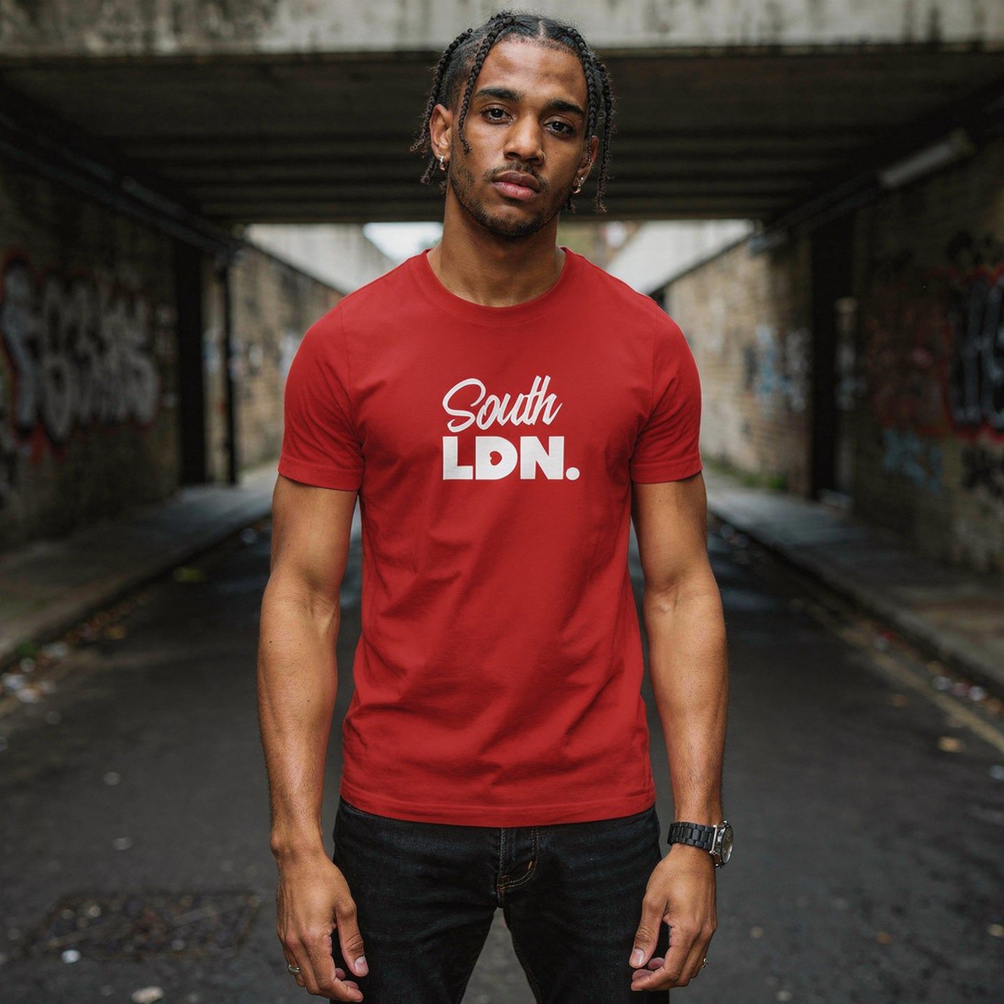 Man wearing a red 'South LDN.' t-shirt standing in an urban alleyway.