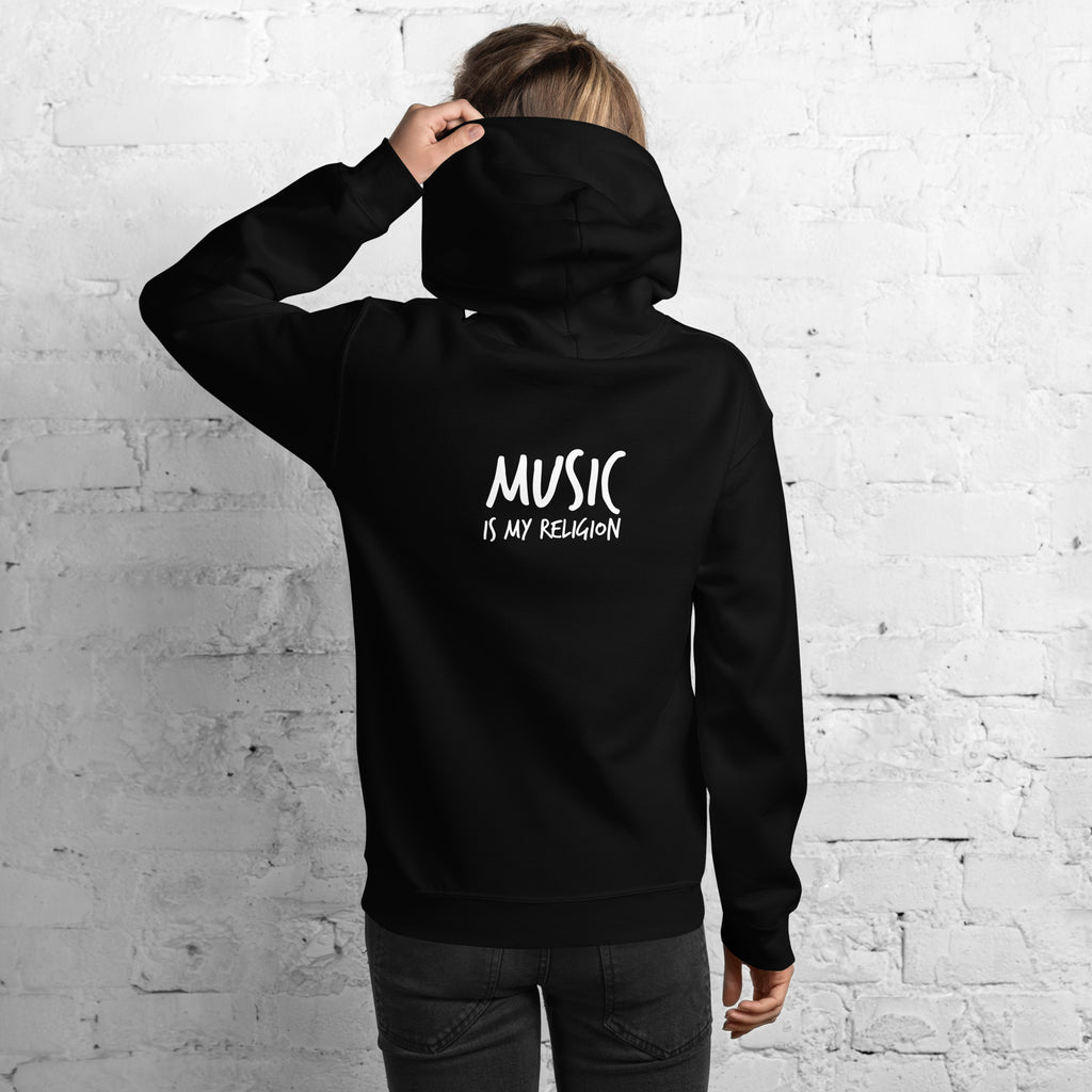 Person wearing a black hoodie with 'Music is my Religion' text on the back against a white brick wall.
