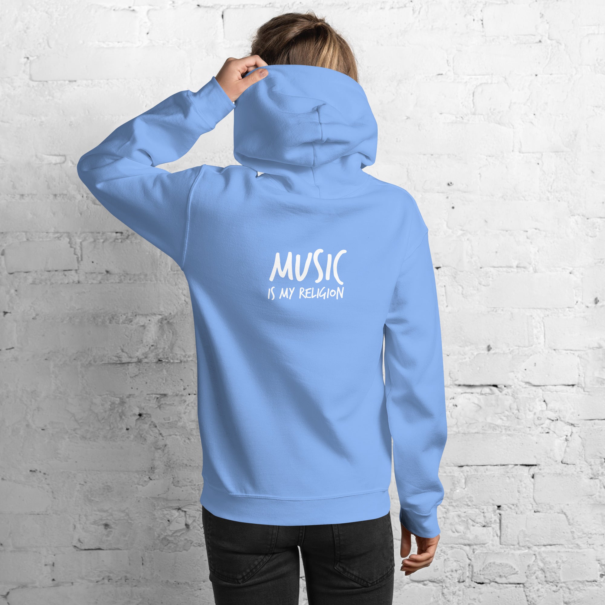 Person wearing a blue hoodie with 'Music is my Religion' text on the back against a white brick wall.