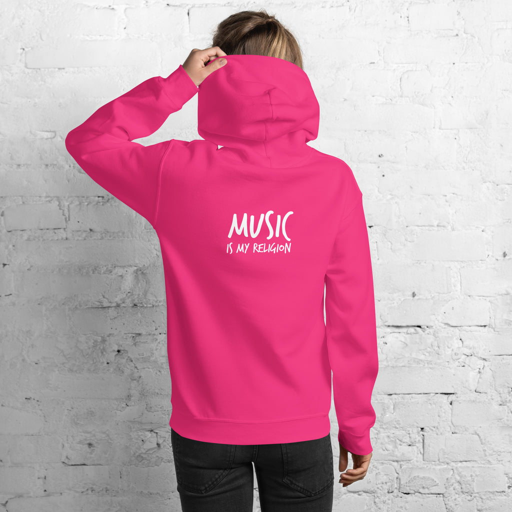 Person wearing a pink hoodie with 'Music is my Religion' text on the back against a white brick wall.