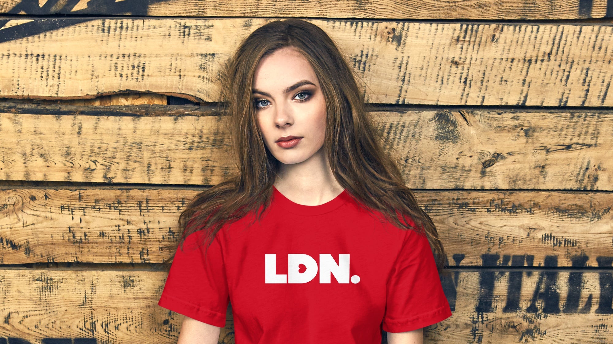 Woman wearing a red 'LDN' t-shirt sitting against a wooden wall with a helmet on the ground.