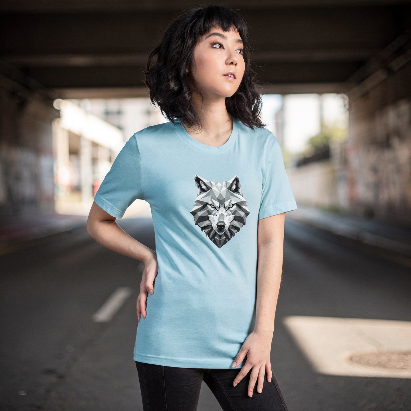 Person wearing a light blue t-shirt with a wolf graphic under an overpass.