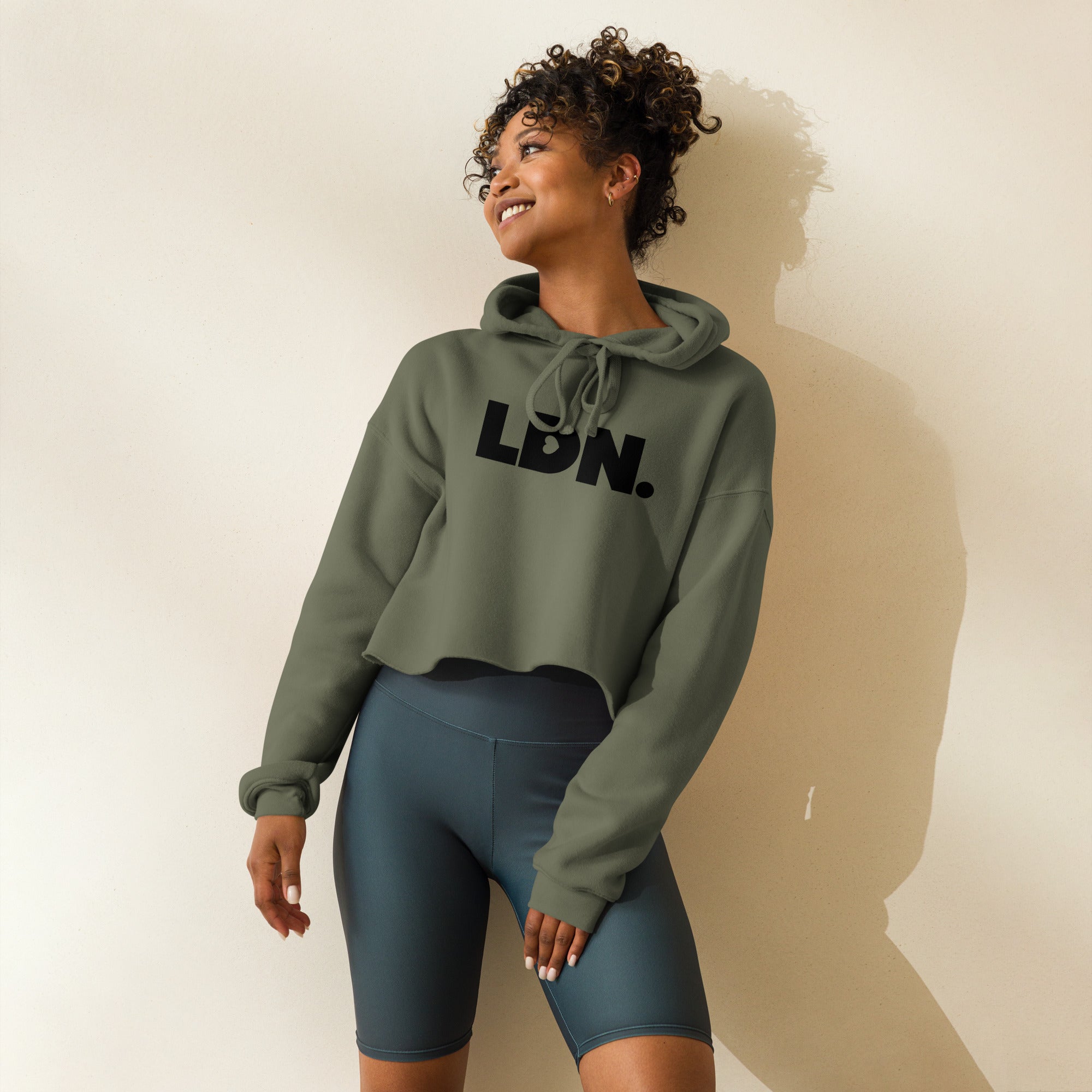 Model wearing a cropped hoodie with tonal “LDN.” graphic. Hoodie features dropped shoulders, raw hem, and dyed-to-match drawstrings. Made from cotton-poly fleece blend for soft comfort and relaxed fit. A minimal, modern streetwear piece.